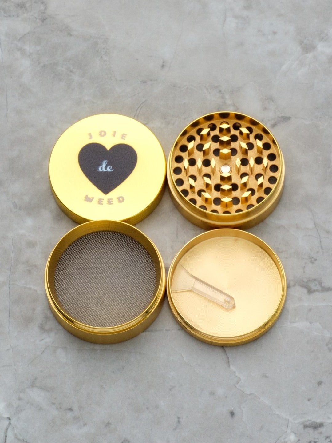 A luxury 4-piece cannabis grinder in a high-shine gole tone finish. The top features the 'Joie de Weed' graphic in black and white, a playful nod to the French phrase 'Joie de Vivre,' - all four pieces of the grinder are laid out.