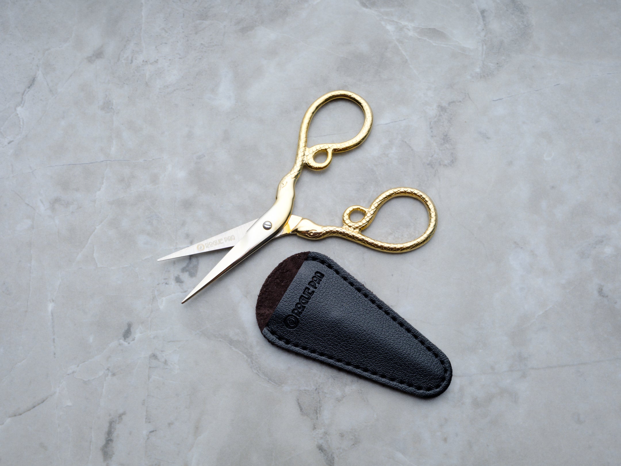 A close-up macro shot of the scissor handles, showcasing the intricate, embossed python scale pattern. The high-polish gold finish over the textured surface creates a reflective, high-fashion aesthetic for the modern cannabis ritual.