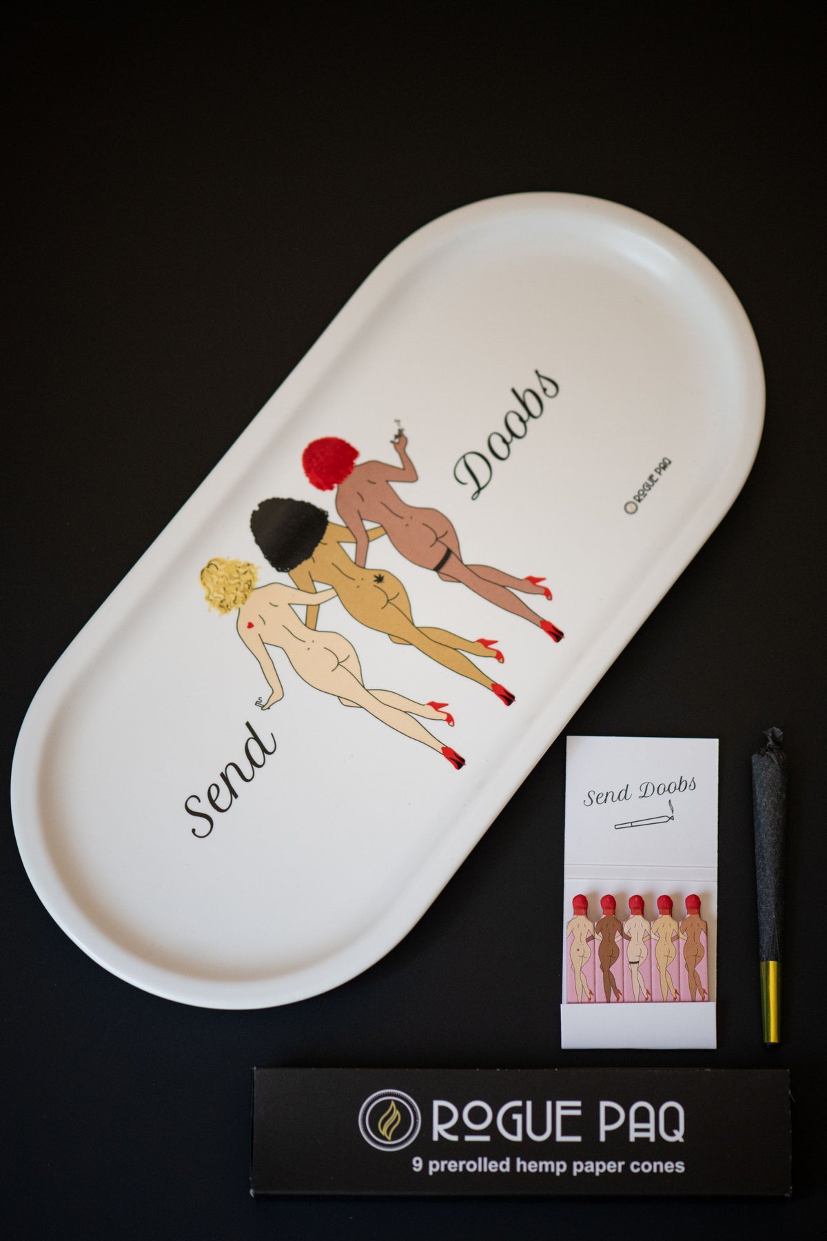 Single book of Rogue Paq SendNudes Matches highlighting the detailed 'Send Doobs' illustration with vibrant colors and retro typography styled with the Send Doobs valet rolling tray and hemp cones.