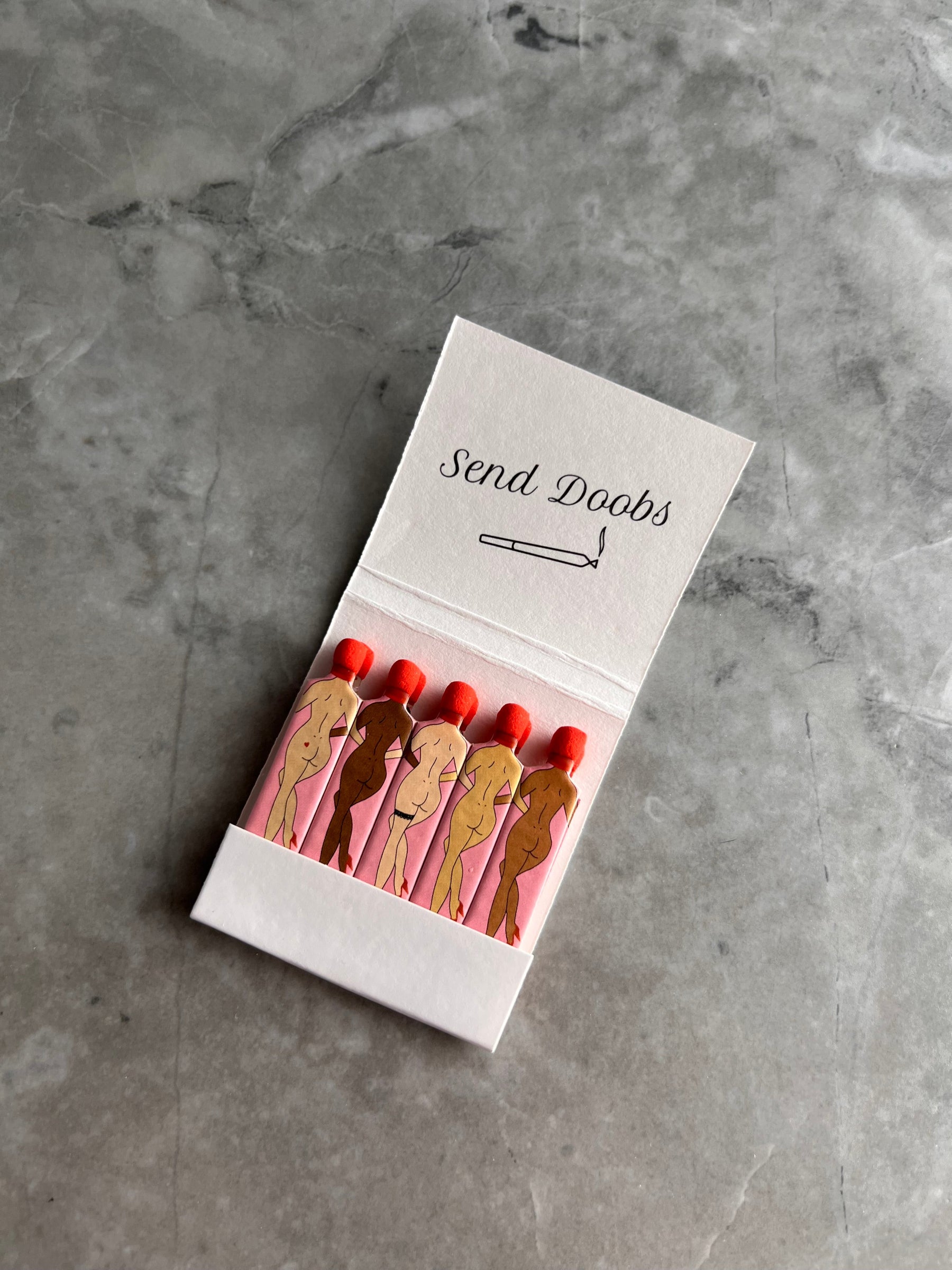 Single book of Rogue Paq SendNudes Matches highlighting the detailed 'Send Doobs' illustration with vibrant colors and retro typography on high-quality cardstock