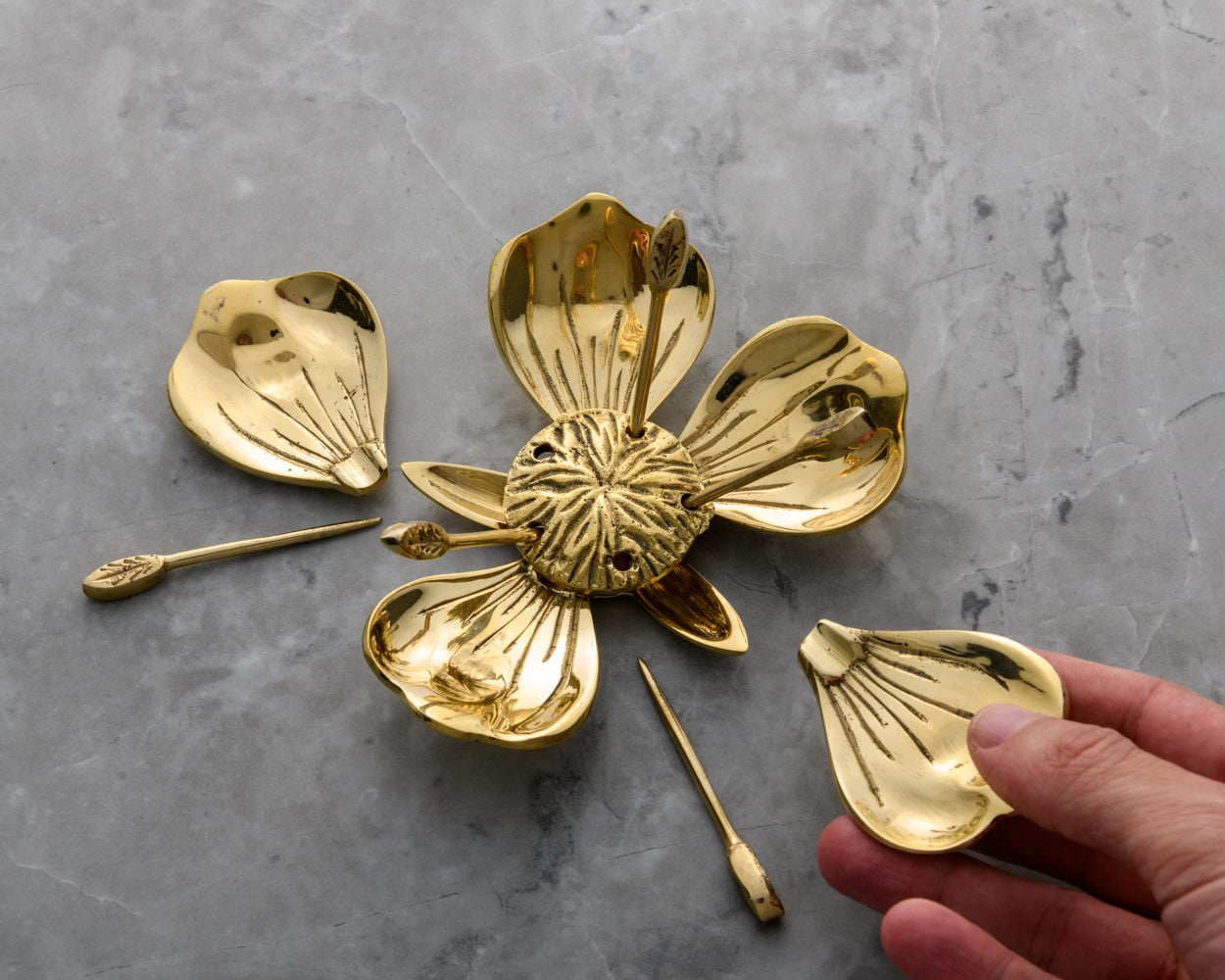 Hand holding a single removable brass petal from the Poppy Party Ashtray; demonstrating the functional design for passing individual ashtrays to guests during a session.