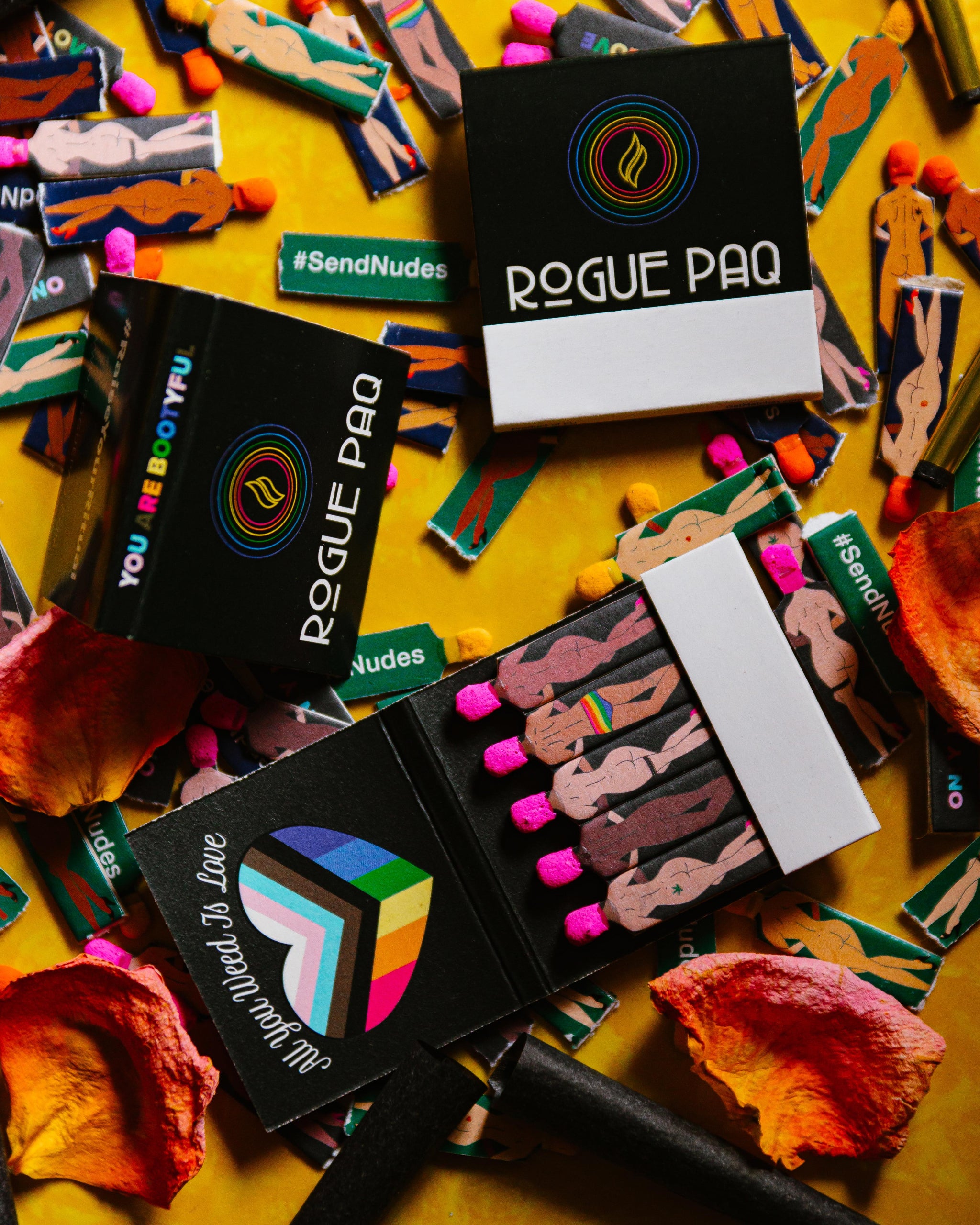 Scattered All You Weed Is Love vintage-style matchbooks featuring diverse figures with the rainbow flag inside a heart; perfect for celebrating Pride or gifting to a cannabis-loving partner.