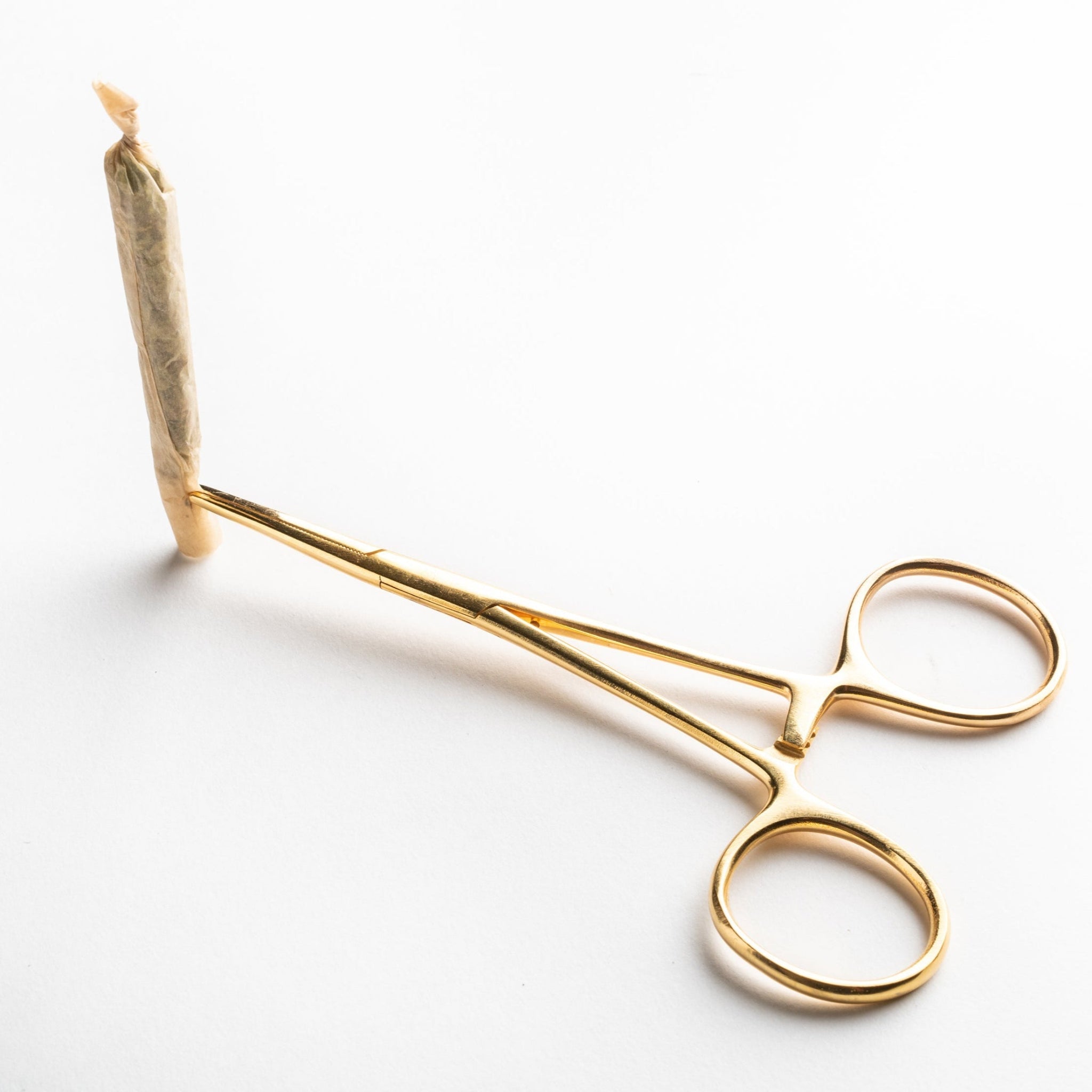 A lifestyle image showing the gold hemostat being used as a jay-clip to hold a hand-rolled joint made with Rogue Paq unbleached hemp papers. This highlights the tool's utility in keeping fingers clean and cool during use