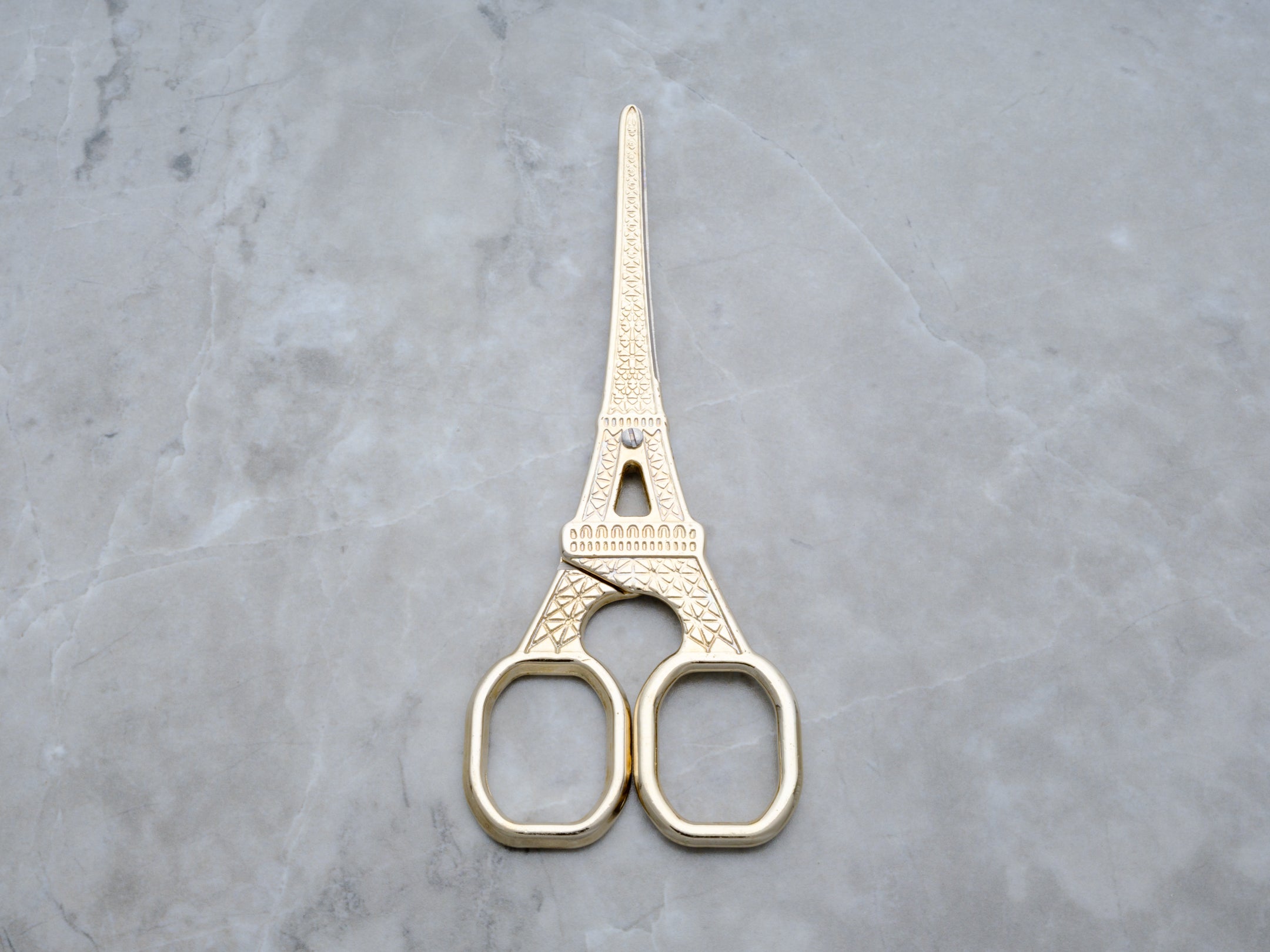 A flat lay shot of the scissor handles, highlighting the intricate latticework and architectural details of the Eiffel Tower design. The high-polish gold finish catches the light, emphasizing the boutique quality of this Rogue Paq accessory.