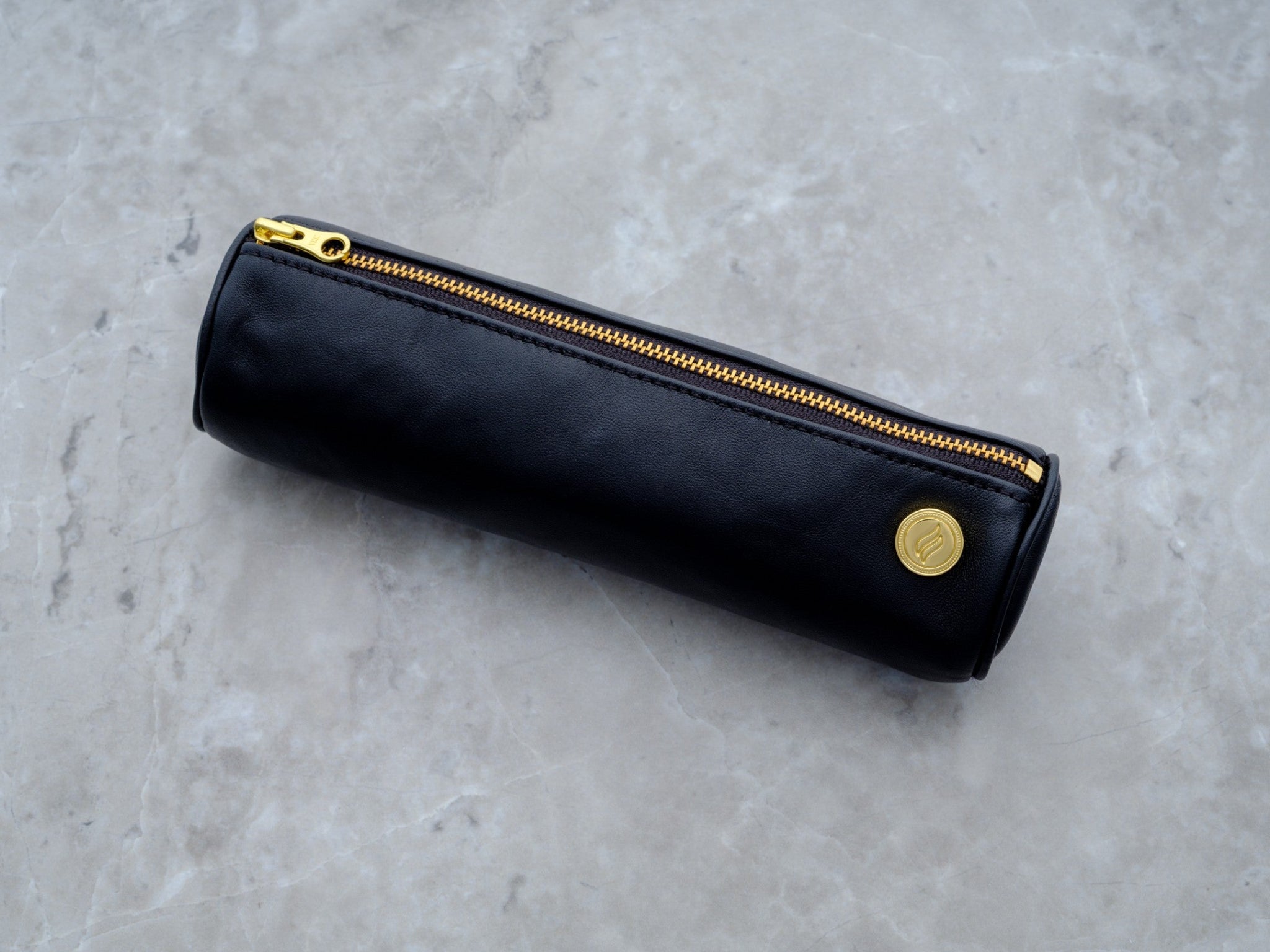 A full-length view of the 8-inch black lambskin Solo Paq. The minimalist design is shown against a neutral gray marble background, highlighting the impeccable stitching and the slim, portable shape designed to corral essentials and keep them safe.