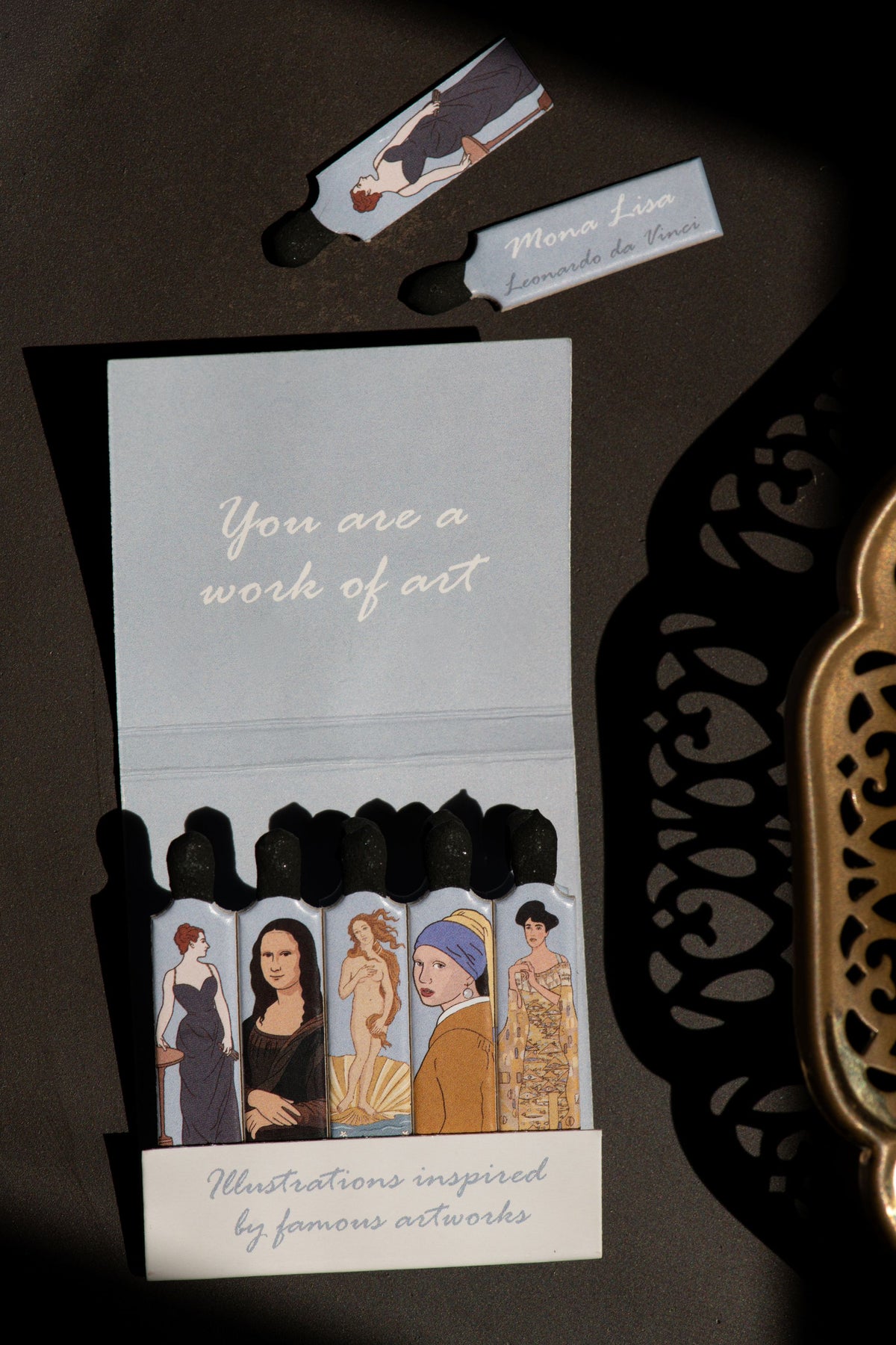 One book of Rogue Paq You are a Work of Art matches styled beautifully next to a gold tray.