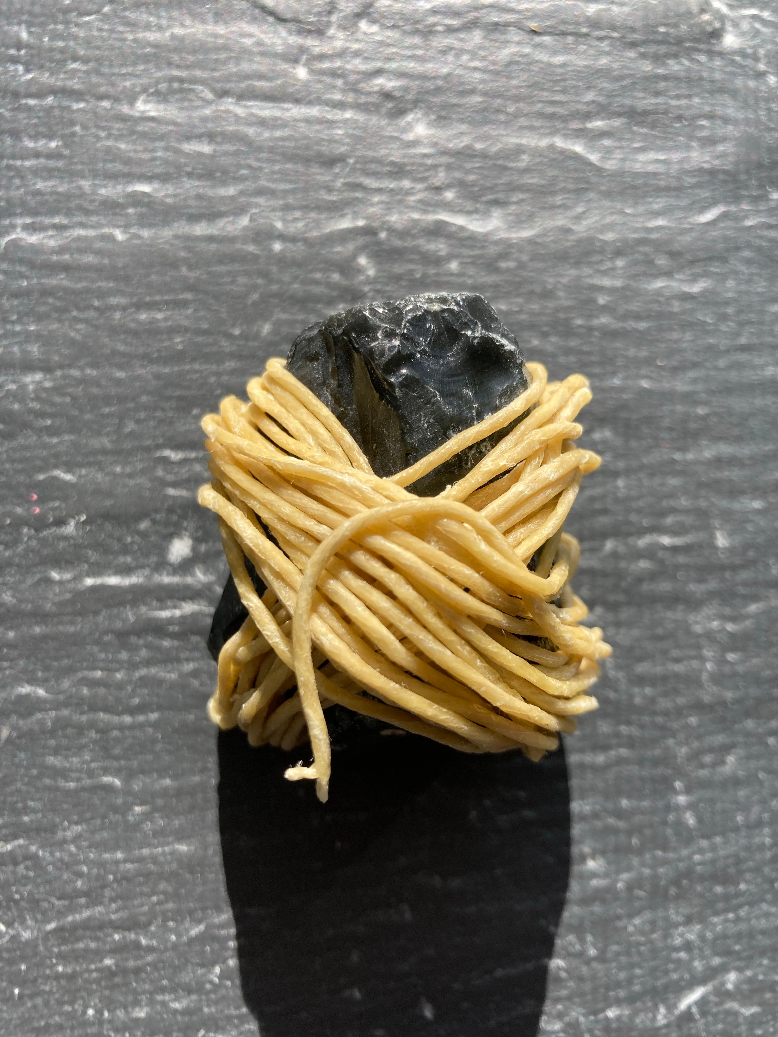 A close-up shot of the Rogue Paq Obsidian Wrapped in Organic Hemp Wick. The 20-foot coil of hemp wick is neatly wrapped around a piece of raw black obsidian showcasing a sophisticated and eco-friendly fire-starting alternative