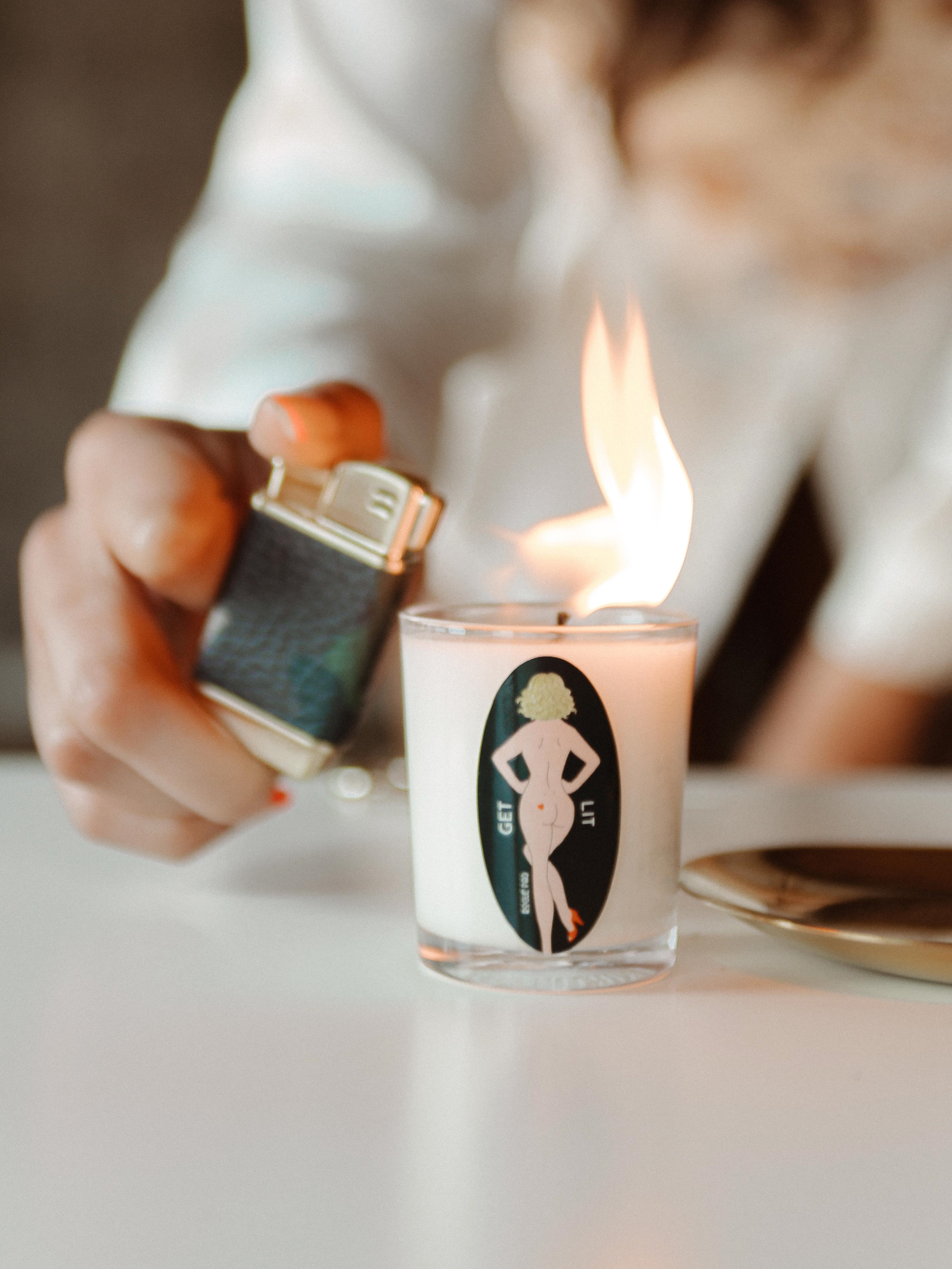 Close-up of the hand-poured organic soy wax of the Rogue Paq GET LIT massage candle, highlighting the natural, smooth texture of the clean-burning wax and the rustic quality of the hemp wick. The candle is being lit with a Rogue Paq refillable butane lighter.
