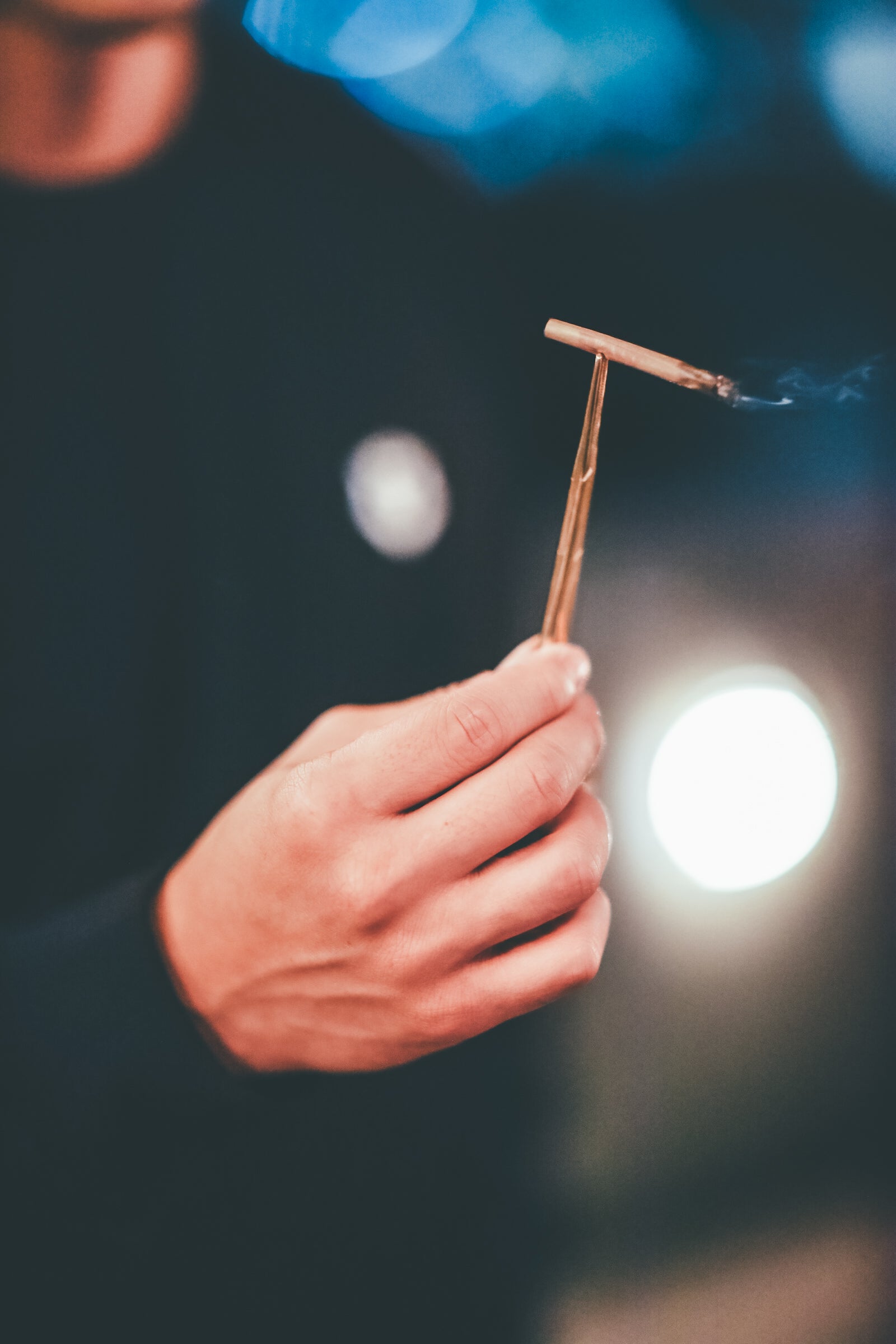 The gold hemostats held between fingers, demonstrating their slender, 5-inch profile. The image showcases the ergonomic finger loops and the reflective metallic finish, illustrating how the tool functions as a clip.