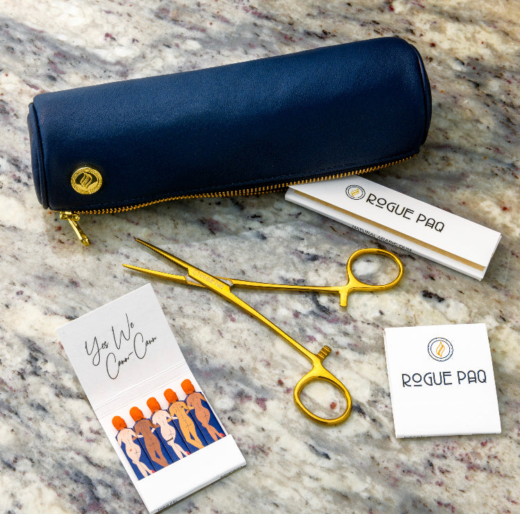 A flat lay of the navy Solo Paq, showing the gold zipper pull and the smooth, fine-grained leather. The image illustrates the case's role as a primary, pared-down carrying solution for a refined cannabis ritual.