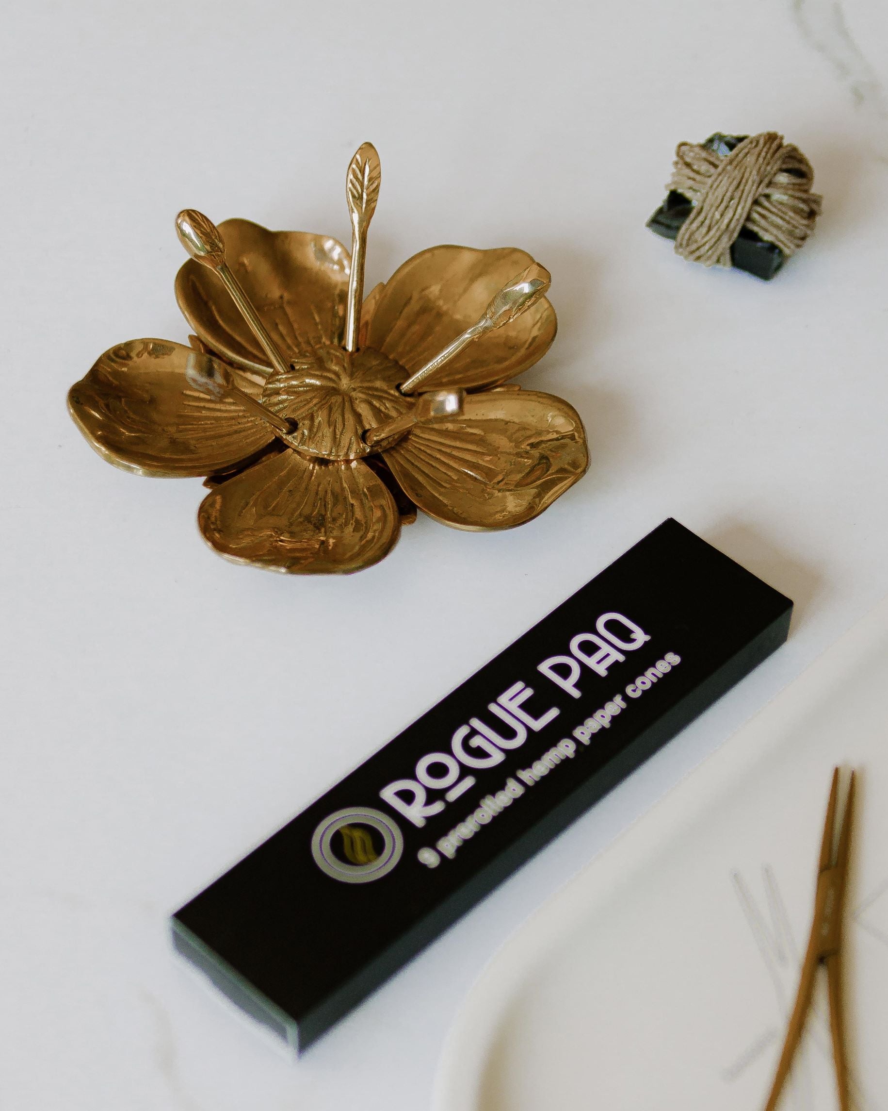 Hemp wick preserves the flavor of premium cannabis flower without butane interference. This wick wrapped around black obsidian stone is pictured with all natural Rogue Paq hemp pre-rolled cones as well as a hemostat joint clip and the Poppy Party Ashtray. The selection is of high end smoking accessories.