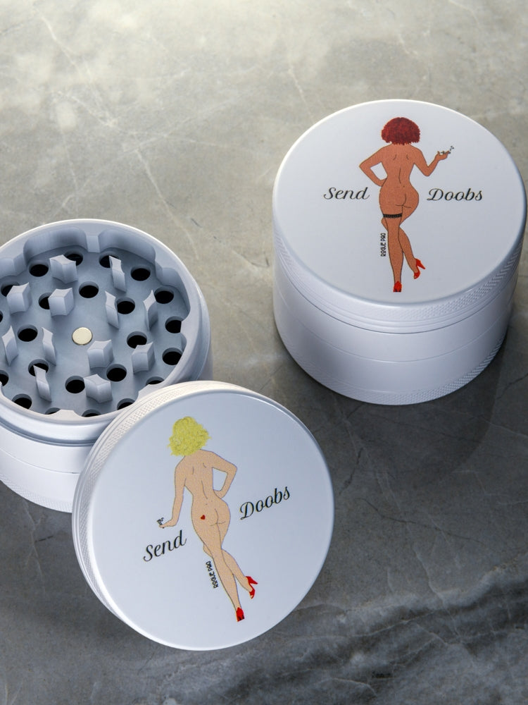 Rogue Paq SendNudes 60mm ceramic weed grinders featuring 'Send Doobs' pin-up art; available in Blonde and Red Head designs with a premium non-stick white finish.