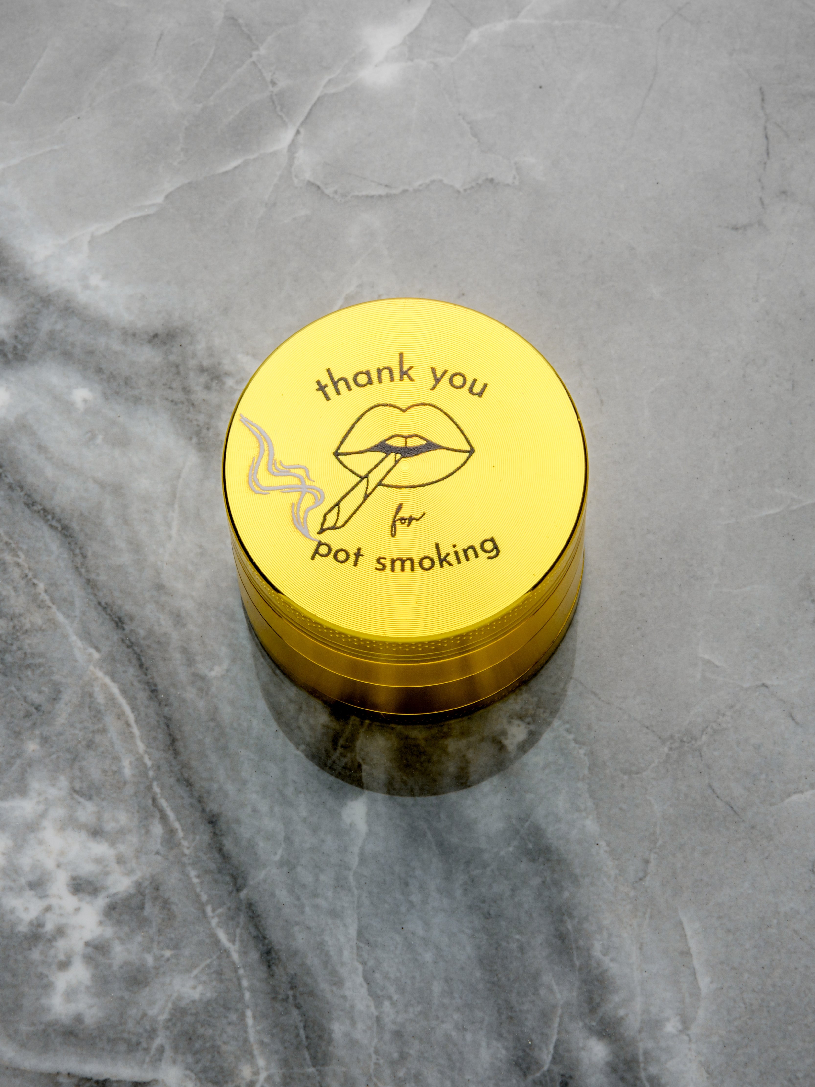 A luxury 4-piece cannabis grinder in a high-shine gold finish. The top features a playful yet sophisticated 'Thank You for Pot Smoking' graphic including lips that are smoking a joint. The Rogue Paq logo is cleanly integrated at the bottom.